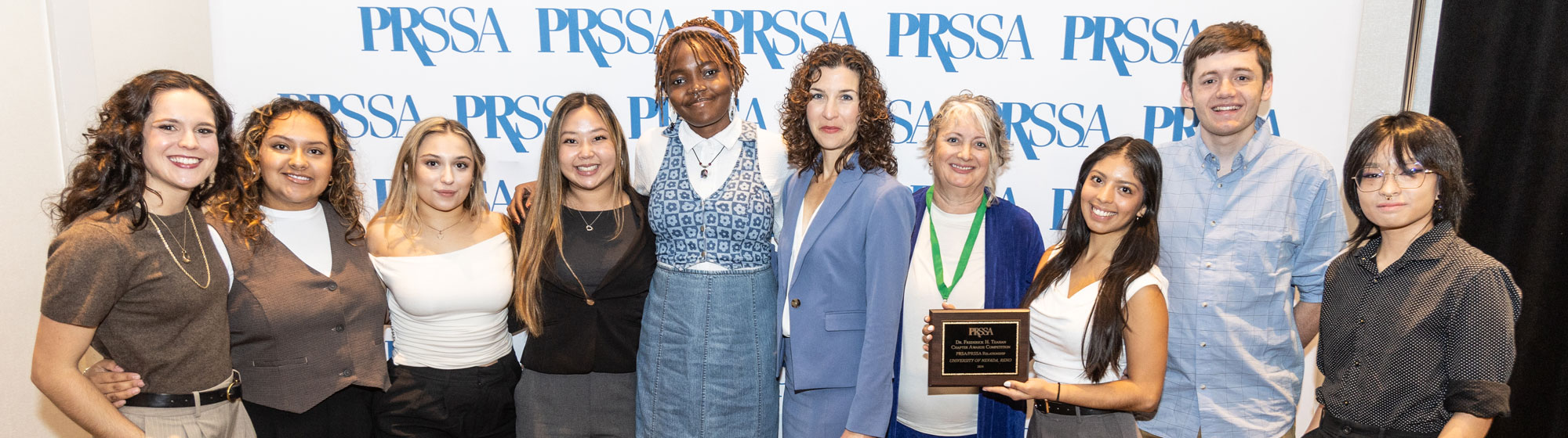 group of students holding award in front of PRSSA logo wall